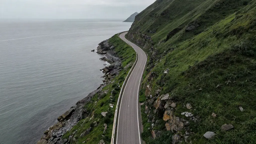Empty coastal road curving along green cliffs above a grey sea
